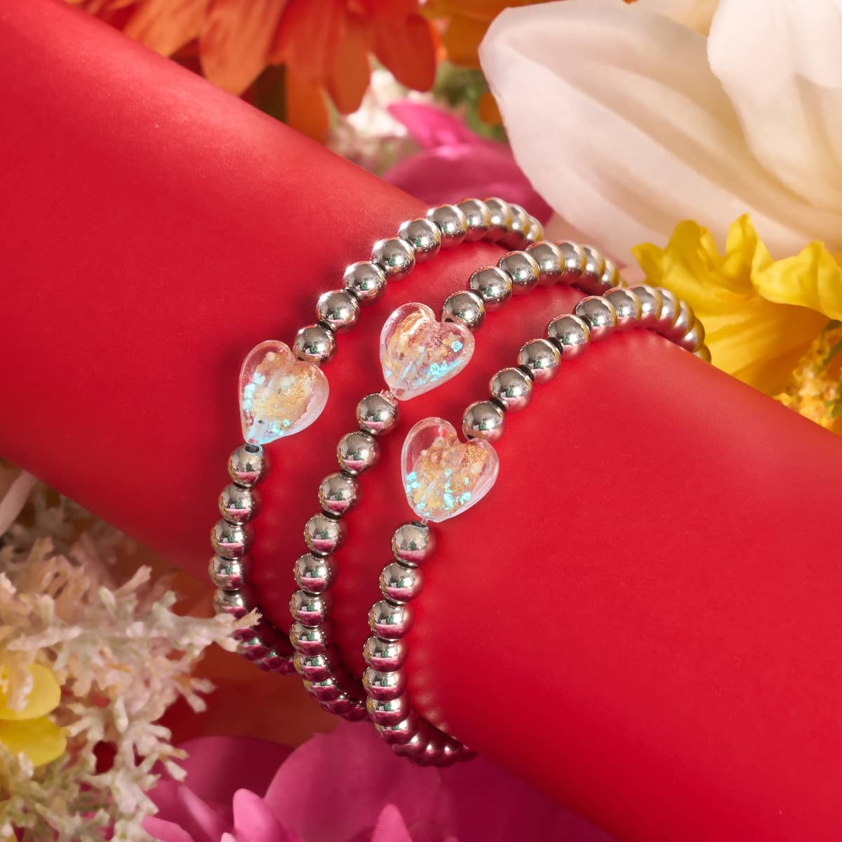 Gilded Pink Glowing Heart Essence Bracelets with silver-plated beads and luminous pink heart charms displayed on red holder with flowers by NOGU